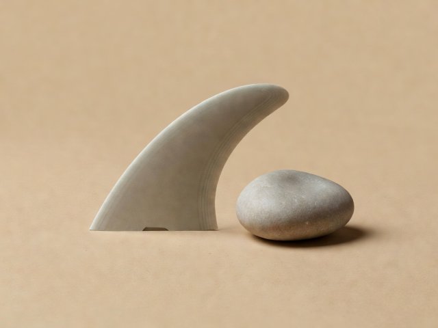 Conceptual 3D render of a surfboard fin beside a smooth pebble